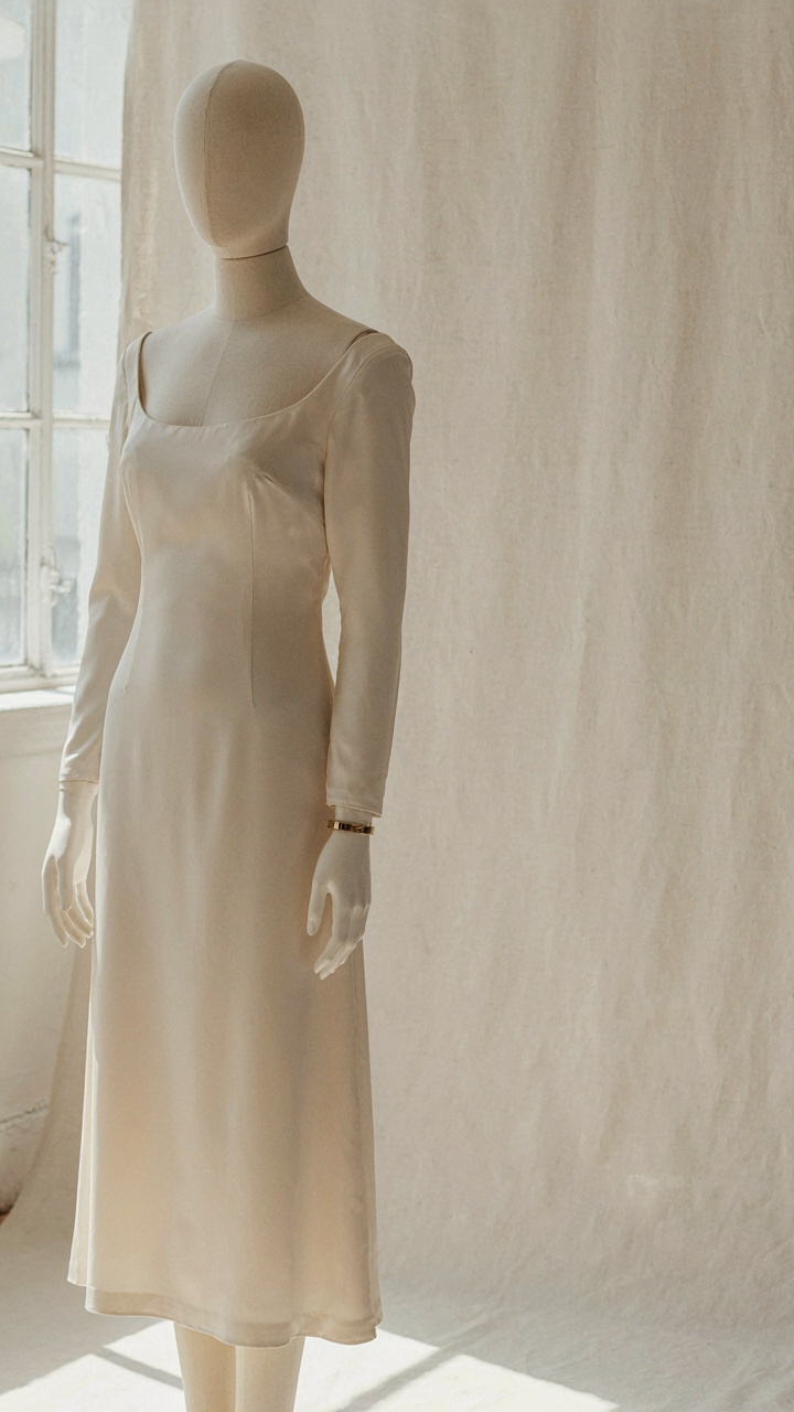 An elegant long sleeve cocktail dress on a mannequin with a single metallic cuff.