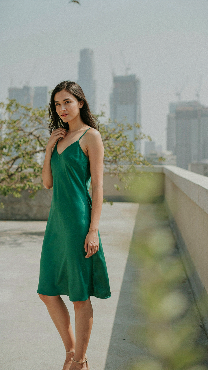 Woman in a vibrant dress stands between blurred branches and a city skyline.