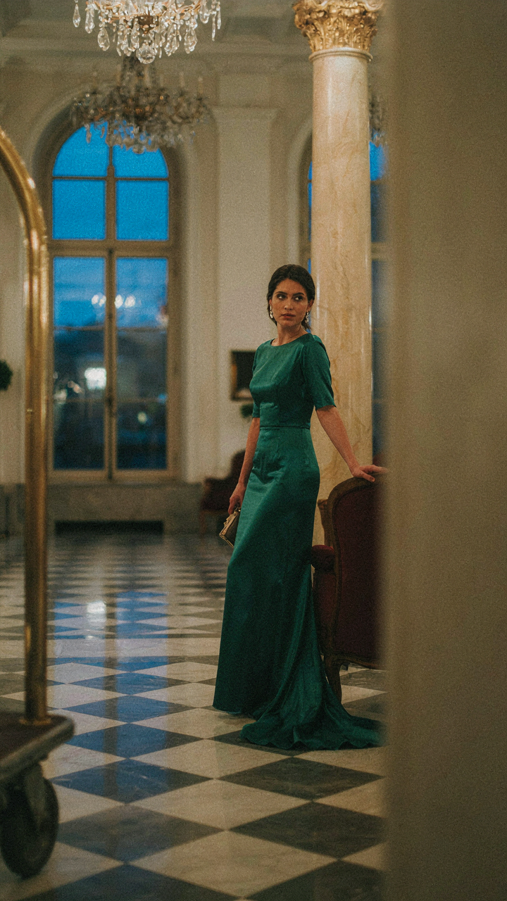 A person in an evening dress stands in a hotel lobby at night.