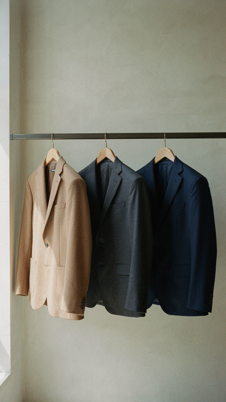 Three different colored blazers hang neatly in a closet, ready for work.