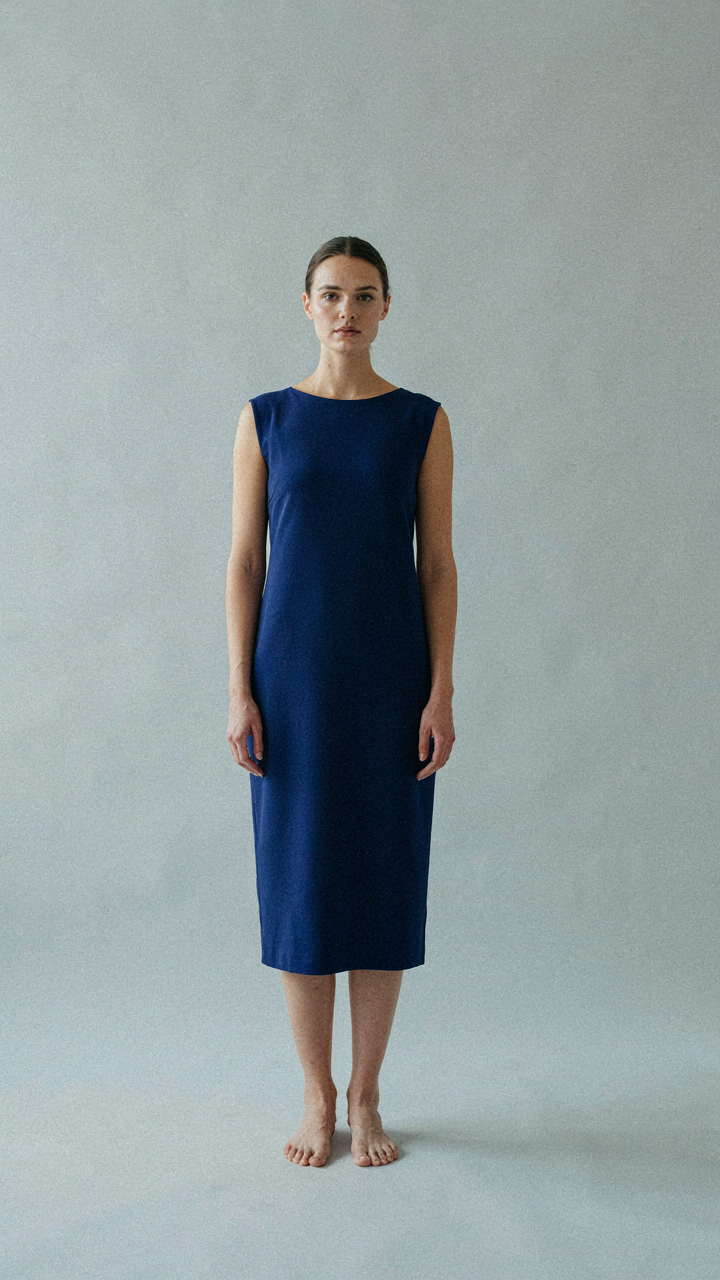 A woman in a deep blue dress stands with perfect posture, fabric hanging evenly.