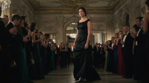 An elegant woman in a black gown walks into a grand opera house.