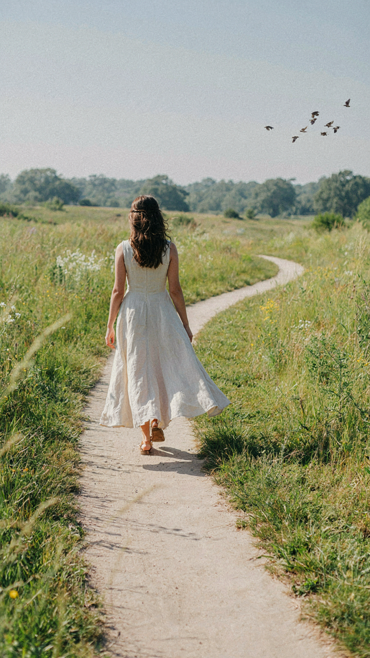 Woman in a long dress walks on a path, fabric flowing in the wind.