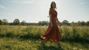 A woman in a beautiful outdoor wedding guest dress walks on a sunny green lawn.