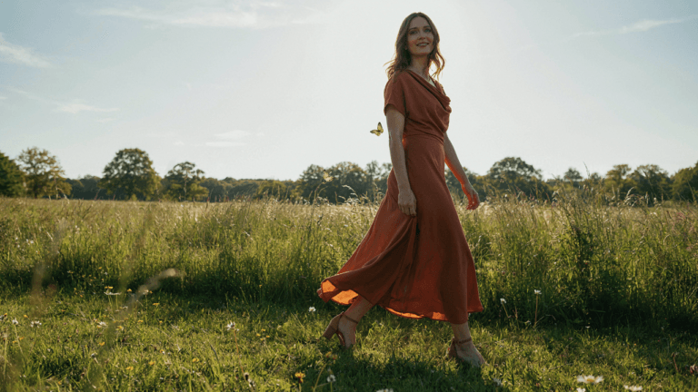 A woman in a beautiful outdoor wedding guest dress walks on a sunny green lawn.