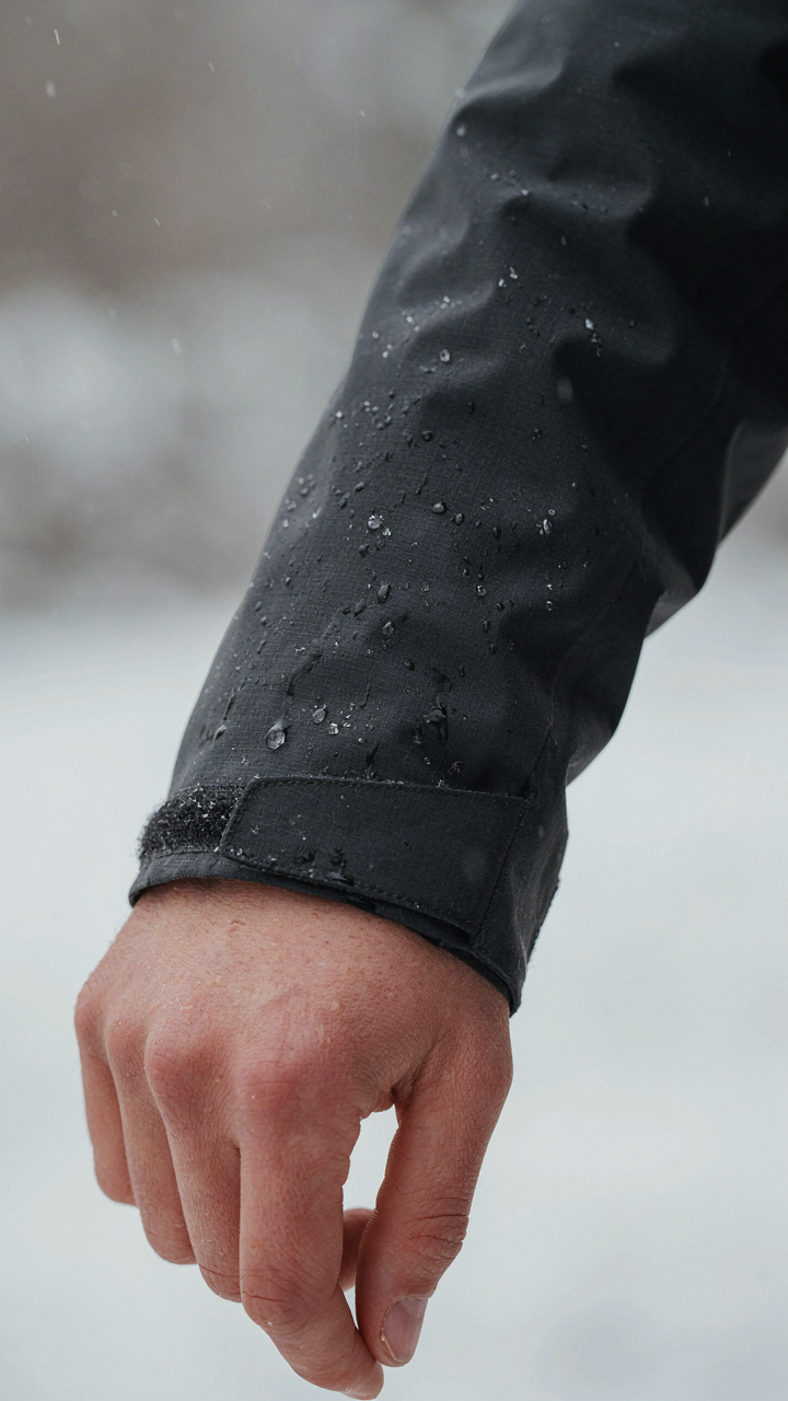 Water beads on a technical shell jacket sleeve during a light snowfall.