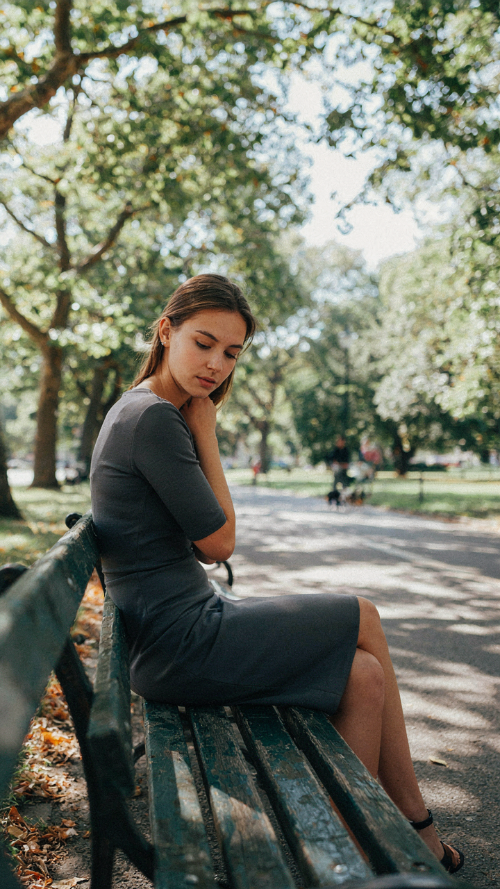 A person sits gracefully on a bench, dress unwrinkled.