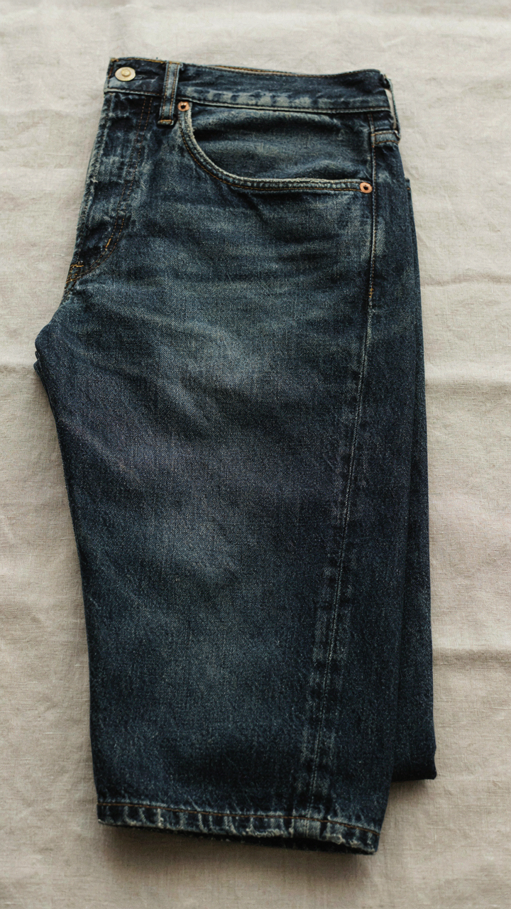 A close-up shows the precise stitching of a well-tailored dark denim jean.