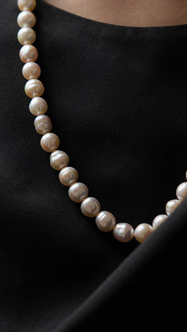 Baroque pearls with texture reflect light against a black cocktail dress.