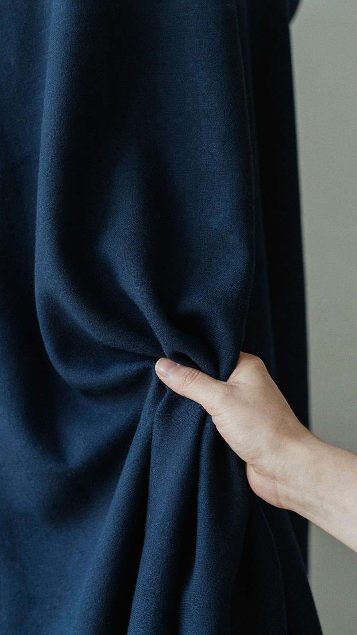 A hand gathers a deep navy, structured fabric that holds its shape.