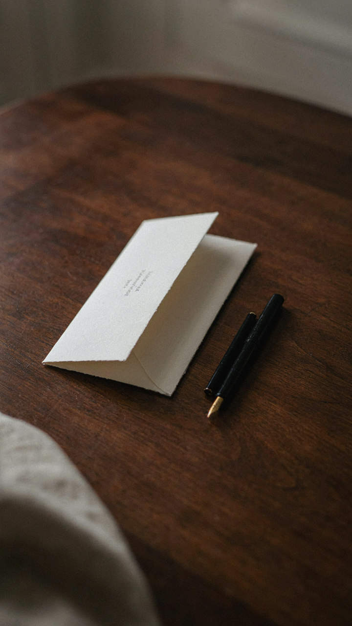 A formal invitation card rests on a polished dark wood table.