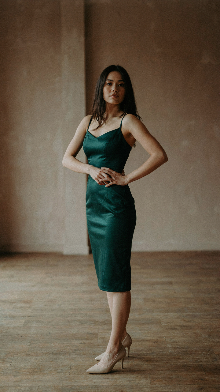 Woman in a cocktail dress poses with weight on her back leg, front leg bent.