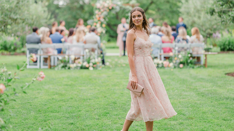A woman in a beautiful rent a wedding guest dress smiles at an outdoor wedding.