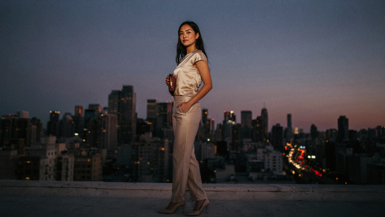 Woman in an elegant satin pants cocktail outfit against a city skyline at dusk.