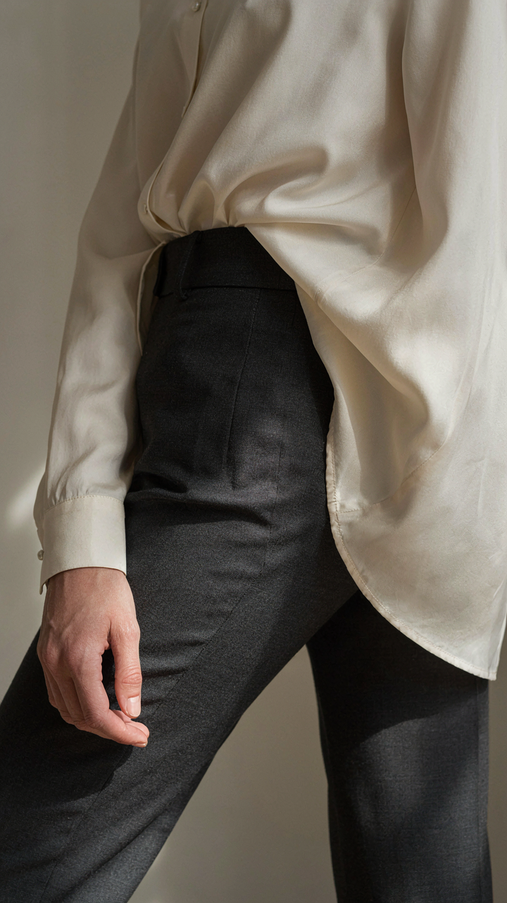 Satin blouse half-tucked into tailored trousers, cuff fastened at the wrist.