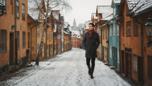 A person walks on a snowy street in a Scandinavian city in winter, wearing a warm coat.