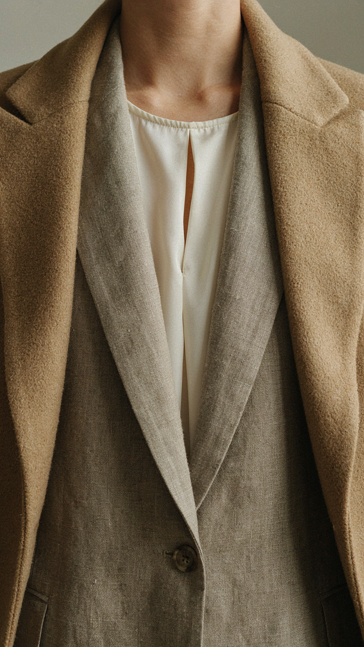Close-up of a layered outfit with cream silk, taupe linen, and camel overcoat.