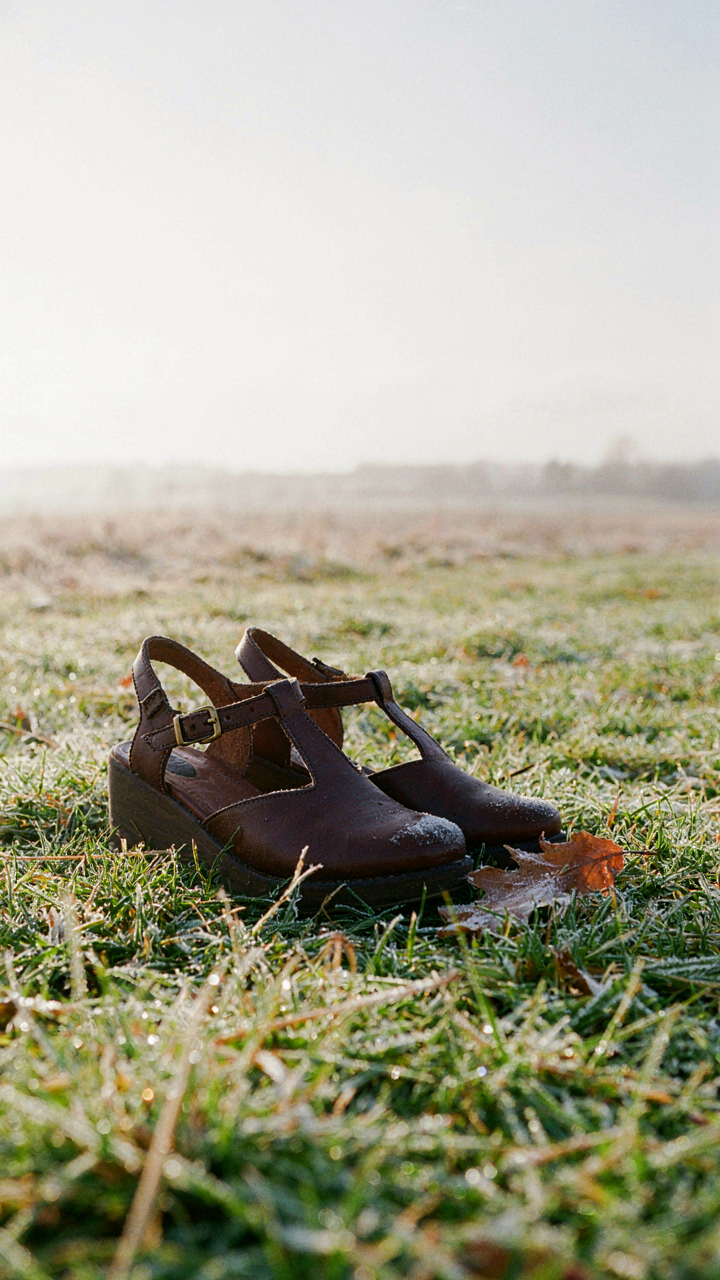 Dark leather closed-toe wedges with textured soles sit on frosted grass.