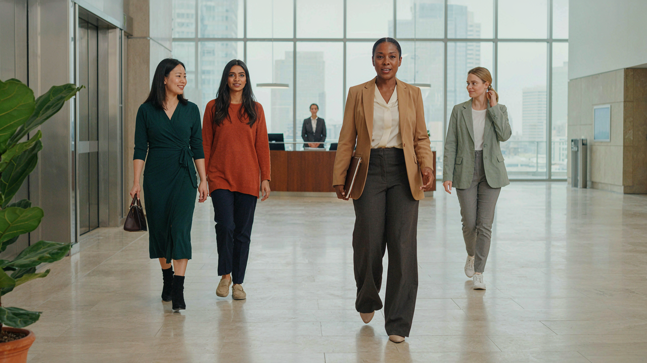 Professional women in diverse semi formal outfits walking through a modern office lobby.