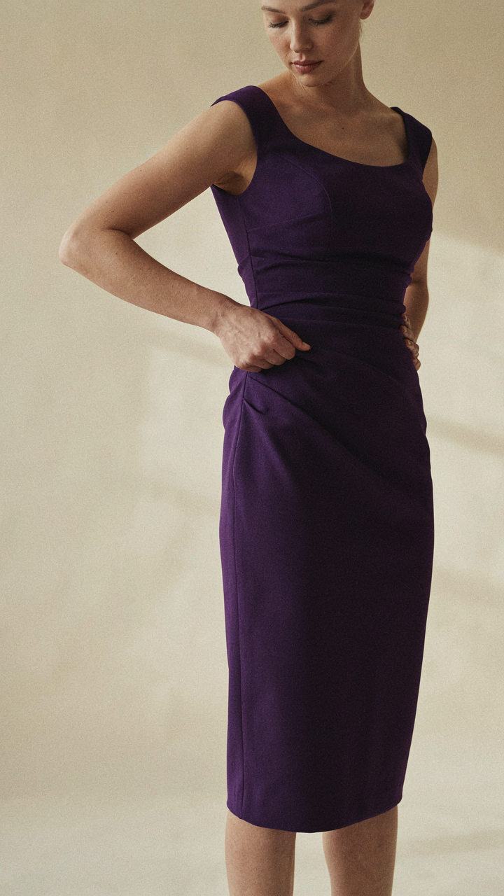 A woman's hand adjusts the ruching on a well-fitted purple sheath dress.