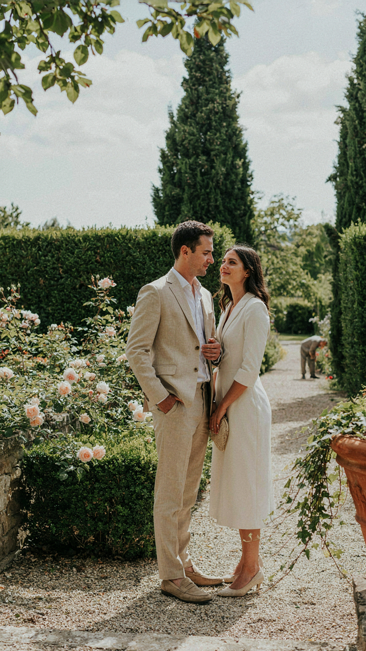 A man in a linen suit and a woman in a midi dress in a garden.