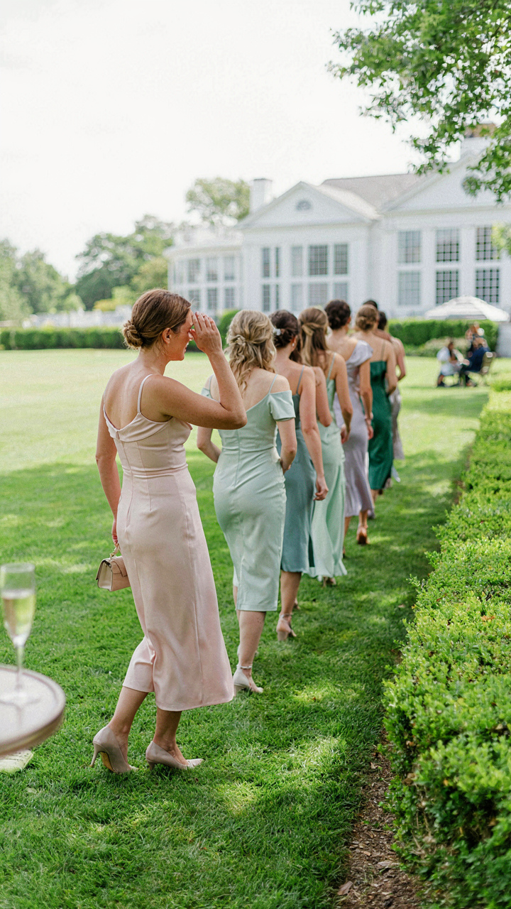 A wedding guest watches bridesmaids in knee-length dresses for dress code cues.