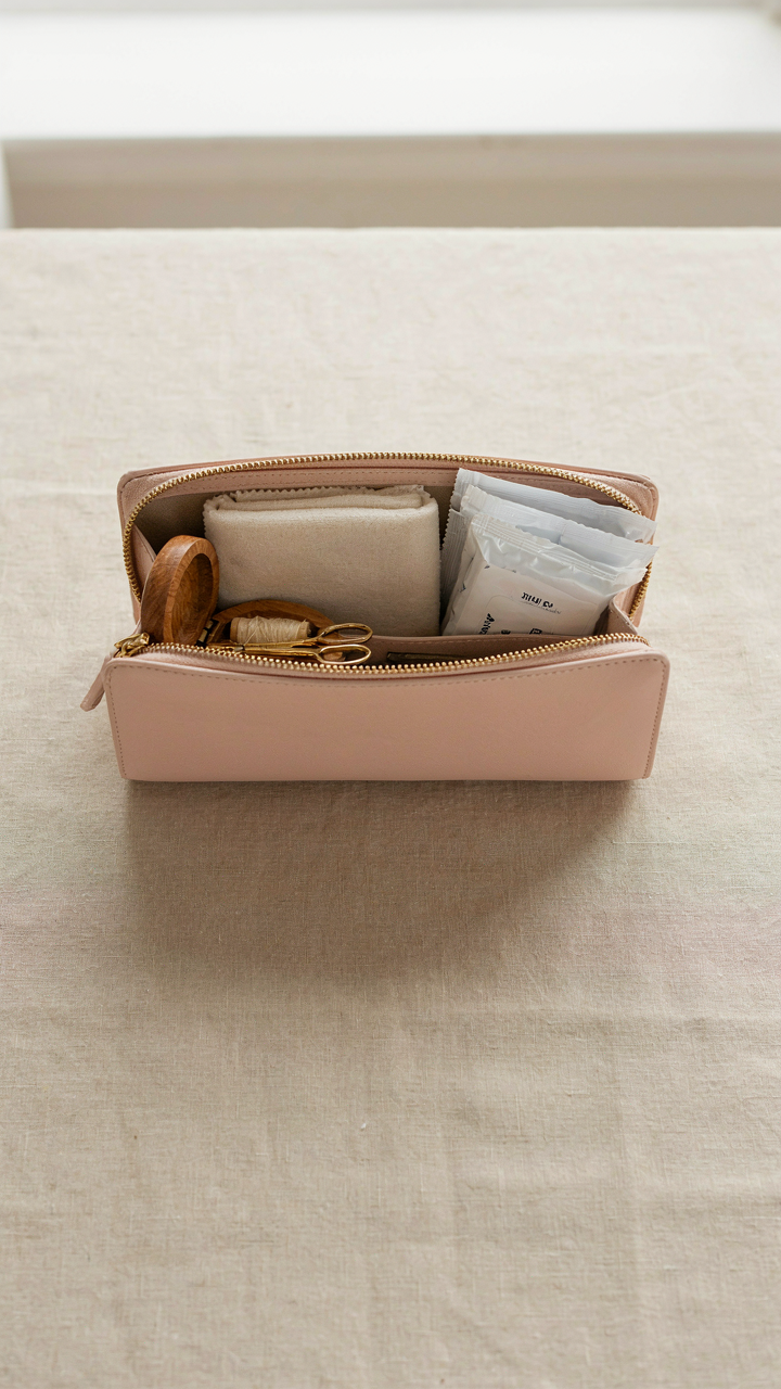 An open clutch bag holds a microfiber cloth, stain remover, and sewing kit.