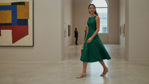 A woman in a cocktail dress walks through an art gallery, showing elegant shoes to wear with a