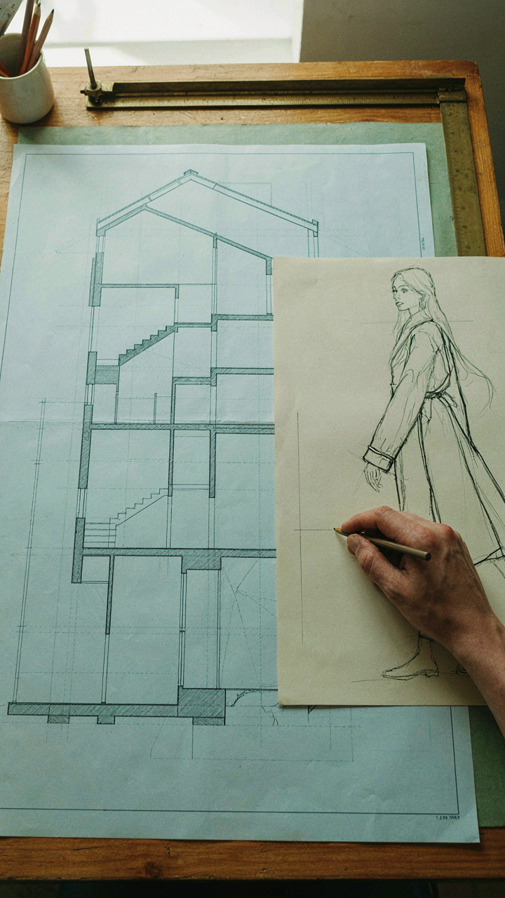 A hand sketches a sleeve on a drafting table, referencing architectural proportions.