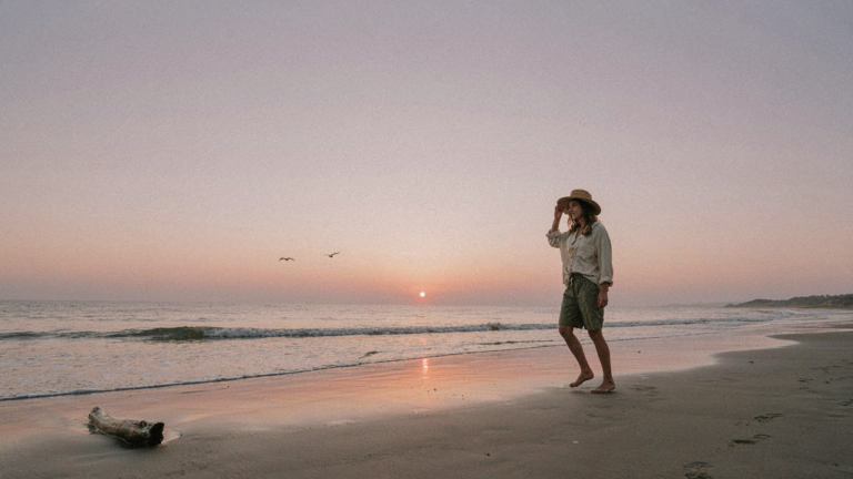 One person in solo beach trip outfits walks on a secluded beach at sunrise.