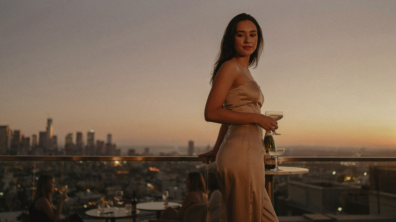 A woman in a stylish strapless jumpsuit evening outfit stands on a city rooftop.
