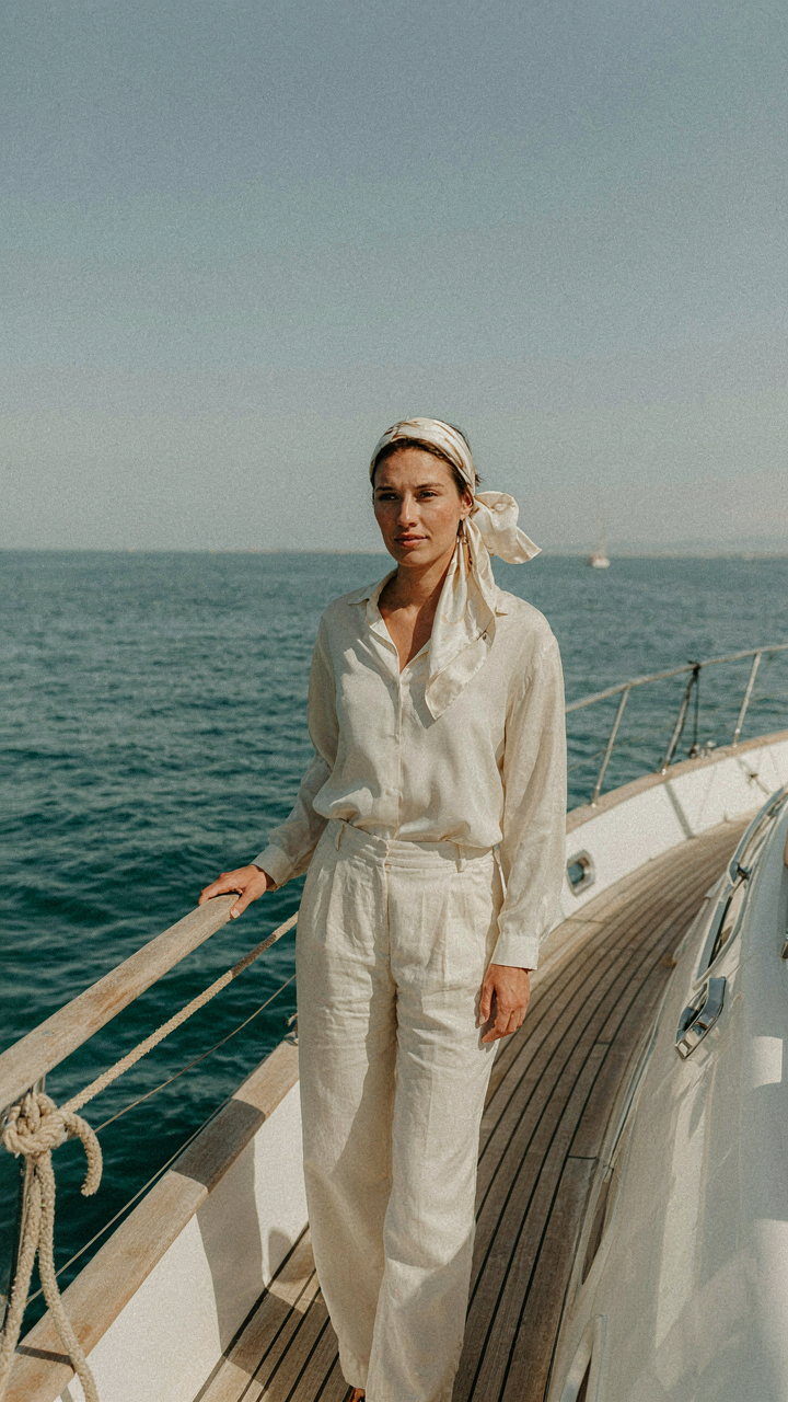Woman in a monochrome cream outfit with a silk scarf headpiece on a yacht.