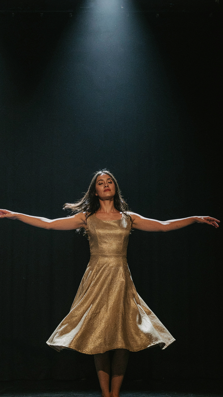 A woman in a gold drop-waist dress dancing confidently under a spotlight.