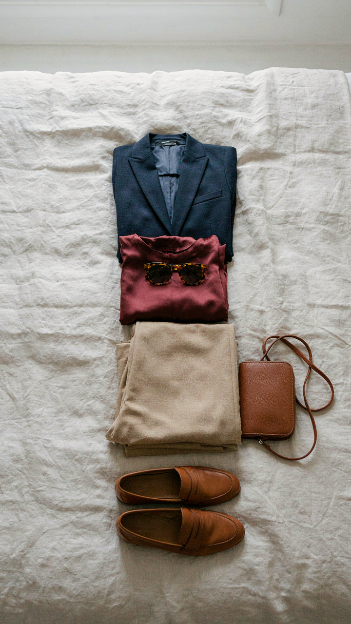 Three clothing items, a navy, burgundy, and beige, arranged on a bed.