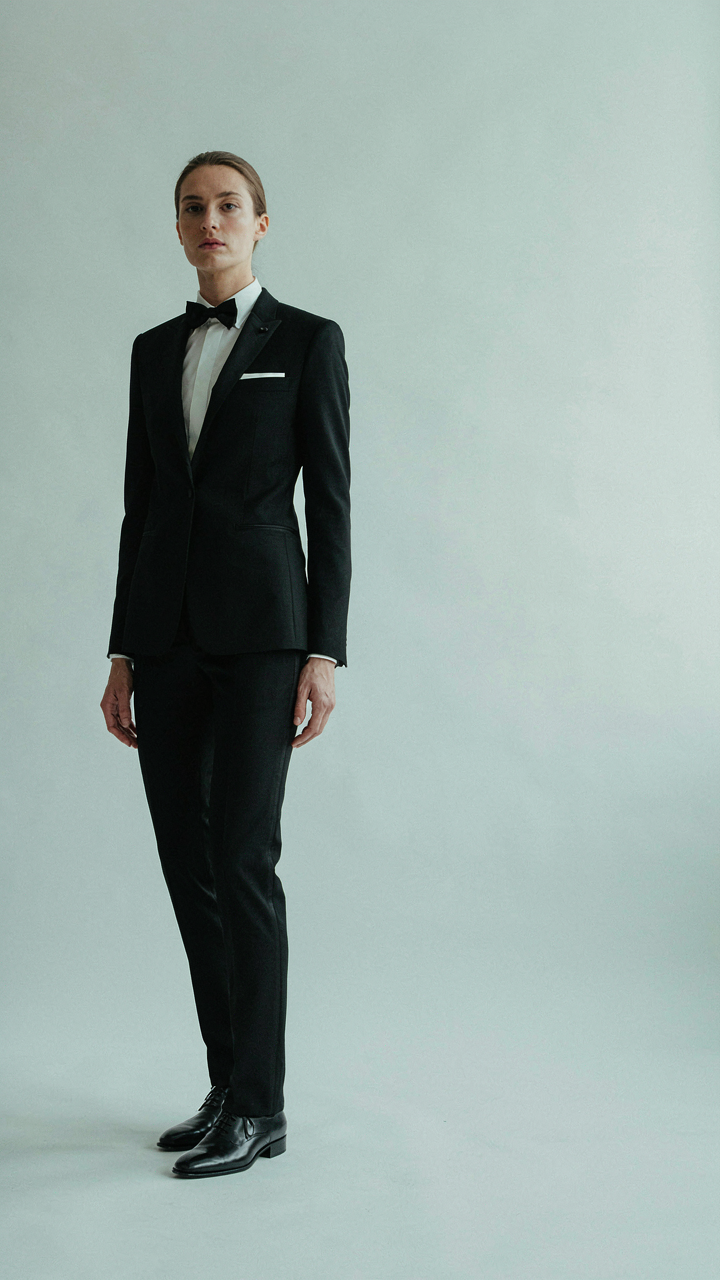 A person in a perfectly fitted tuxedo dress, showing precise tailoring details.