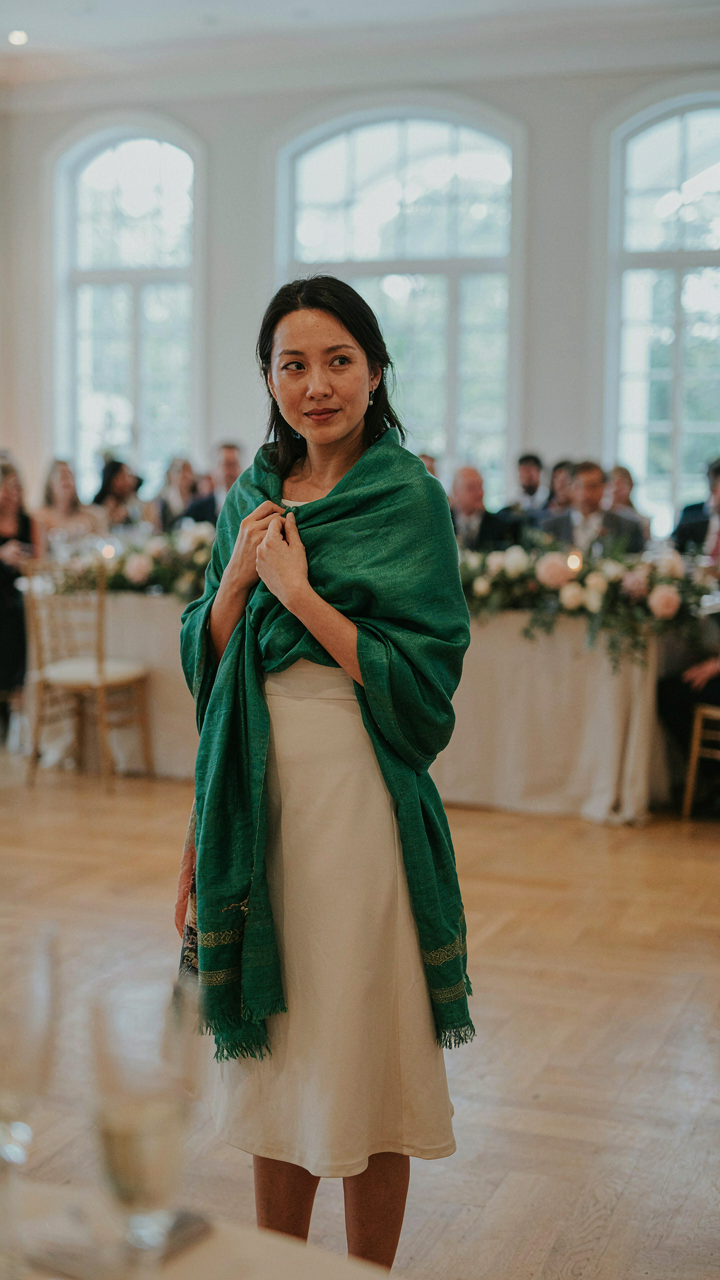 A woman in a neutral dress wears a vibrant jewel-toned shawl for a wedding.