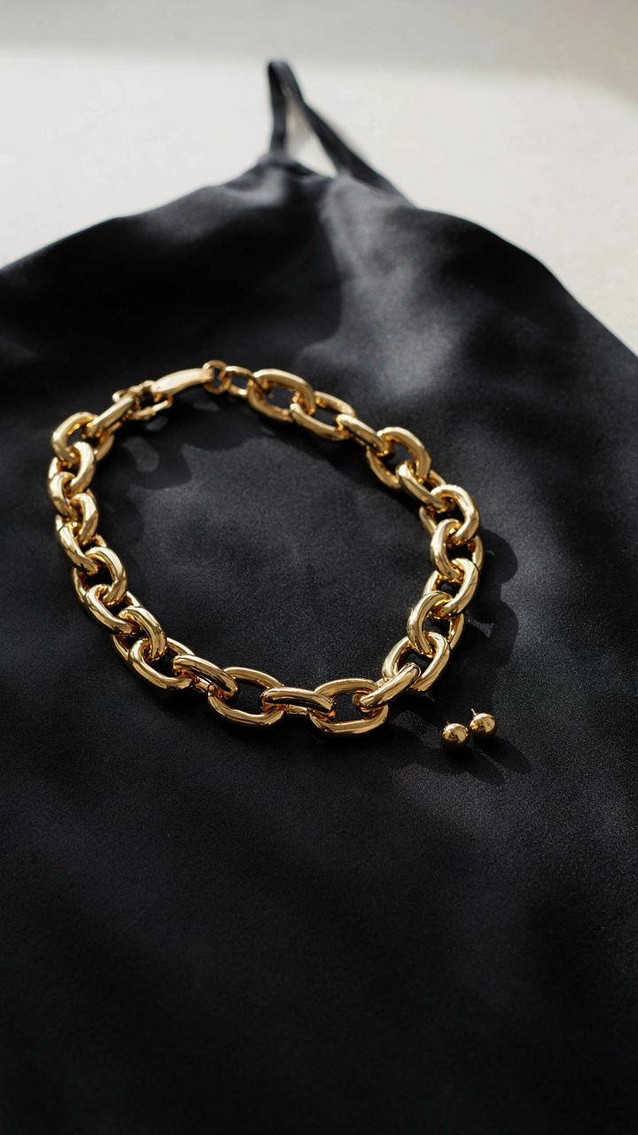 A gold statement necklace rests on a black dress, with simple earrings.