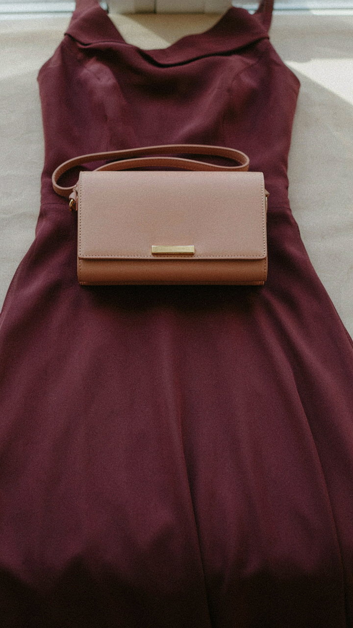 An elegant structured clutch bag rests on a deep plum maxi dress.