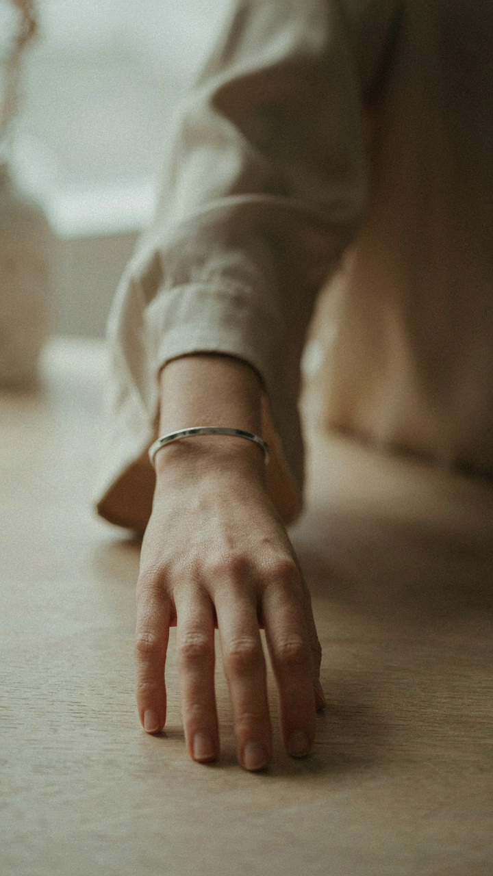 A woman's bare wrist with a single metal cuff, near a satin blouse.