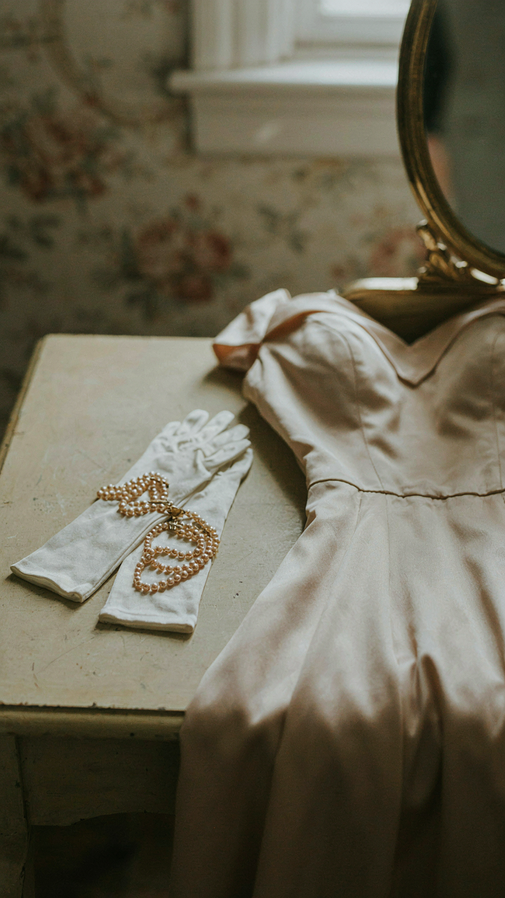Long white opera gloves and a multi-strand pearl necklace next to a dress.