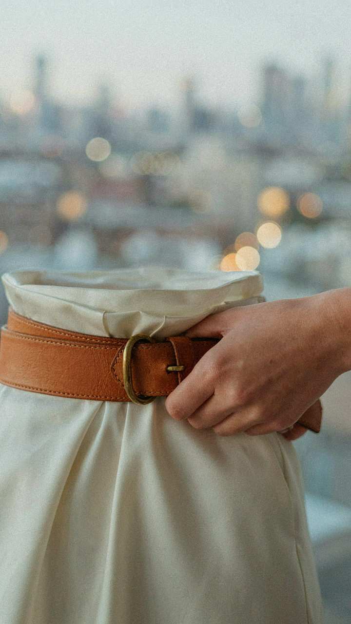 A hand fastens a wide leather belt tightly around a dress.