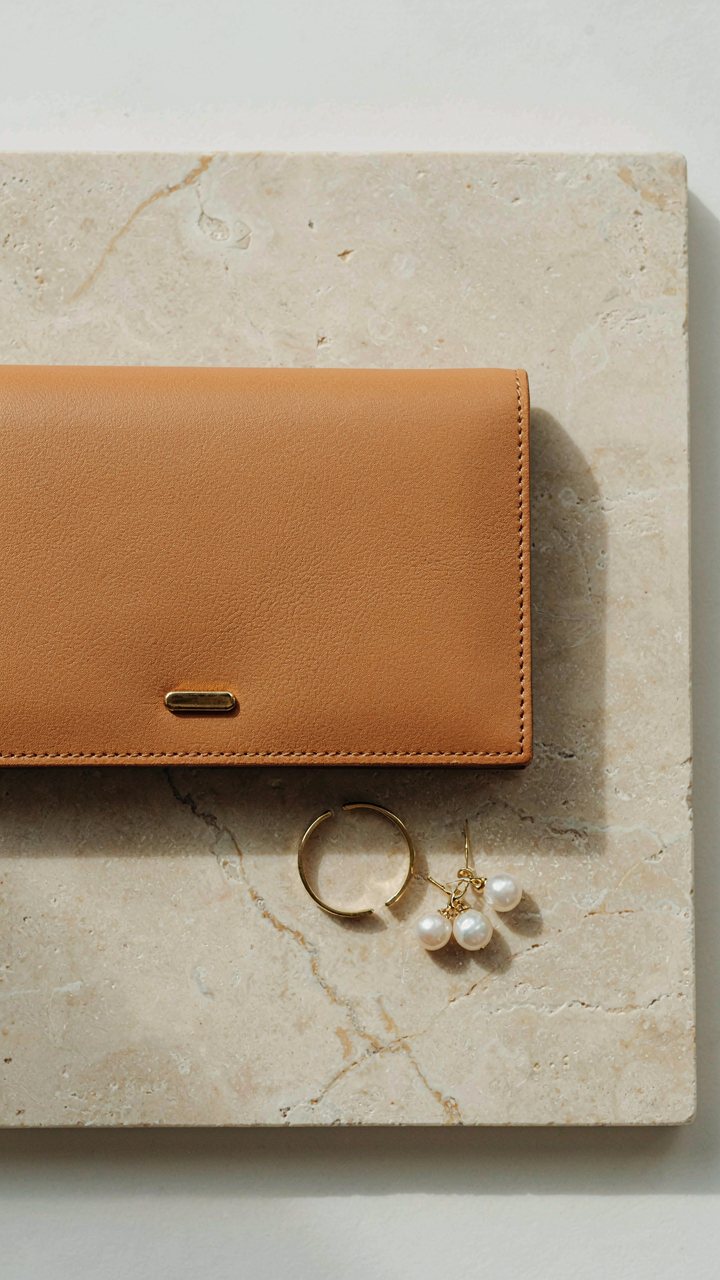 A selection of structured leather clutch, gold cuff, and pearl earrings.