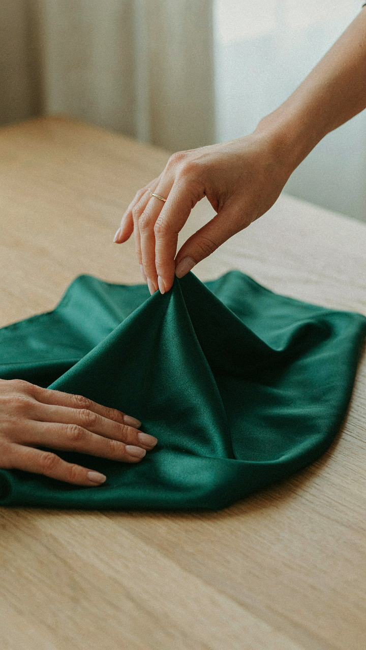 A hand testing the feel of a silk charmeuse fabric swatch.