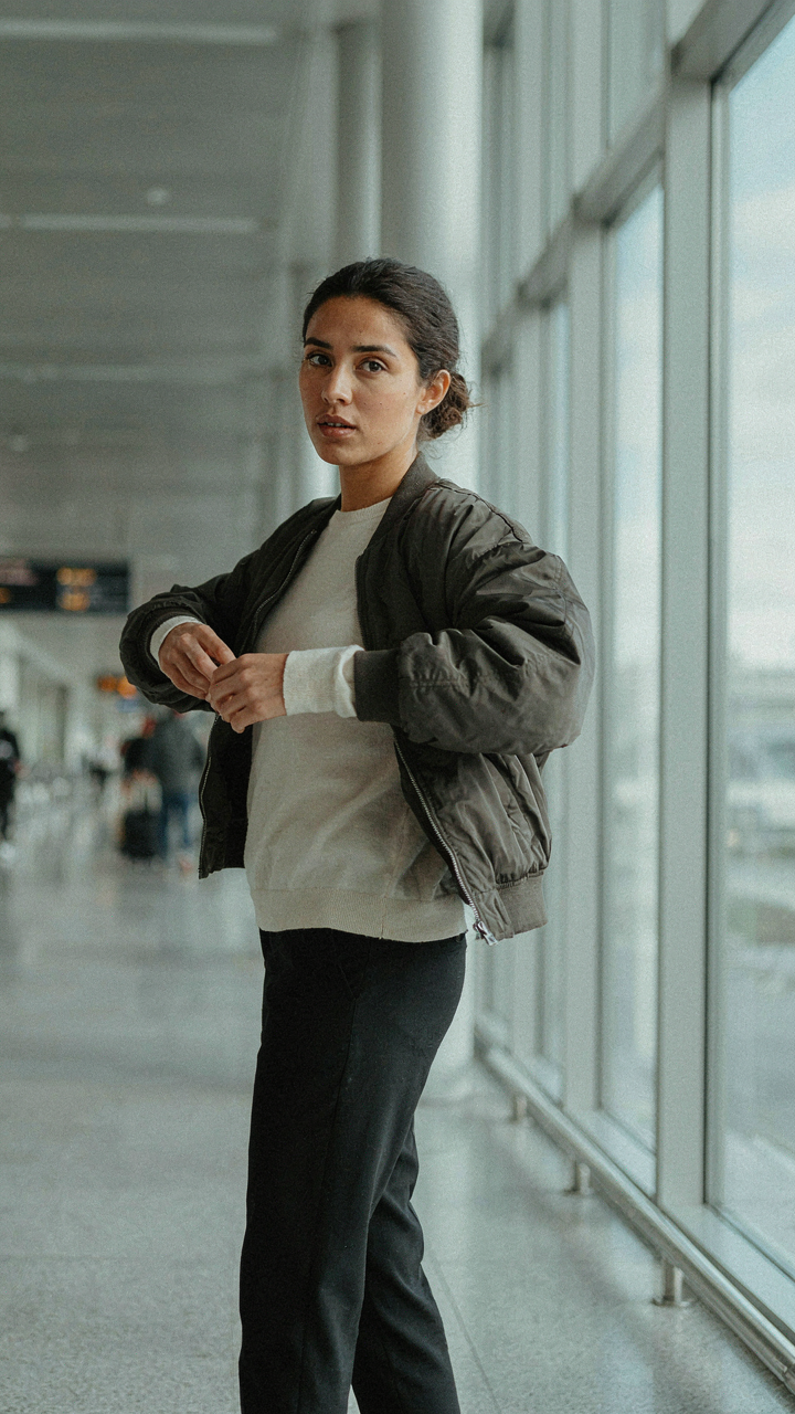 A woman in an airport removes her bomber jacket, revealing a long-sleeve merino shirt.