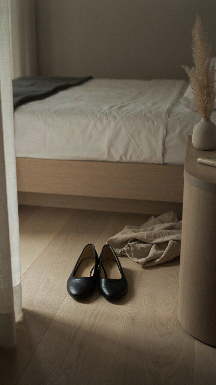 A comfortable pair of black ballet flats sits next to a bed in a hotel room.