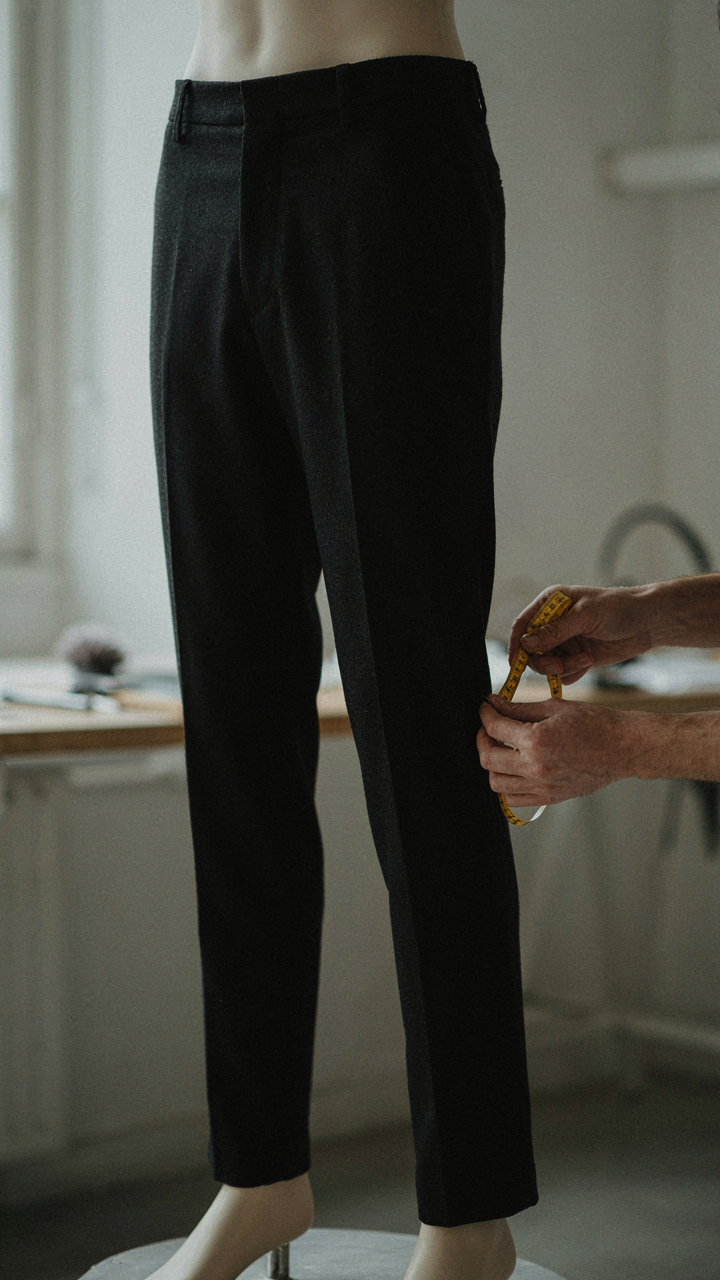 A tailor's hands adjust the hem of black trousers, ensuring perfect proportion.