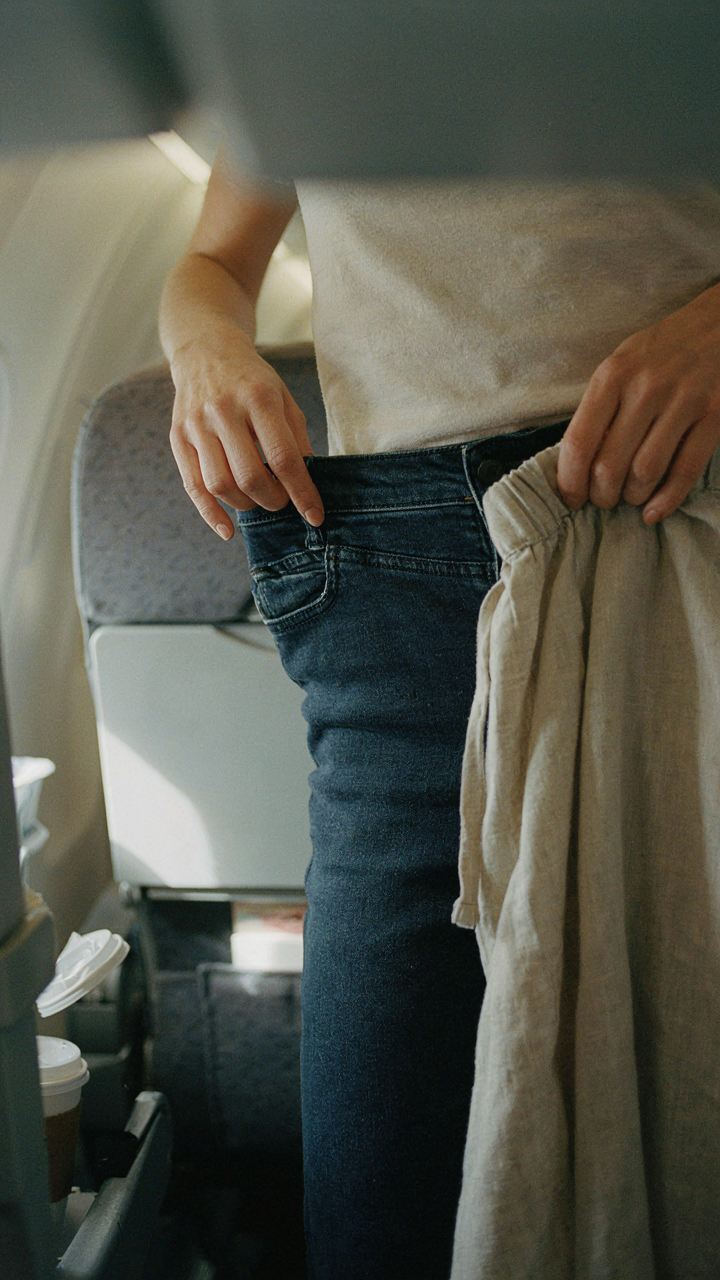 Woman swapping tight jeans for comfortable linen pants on a long haul flight.