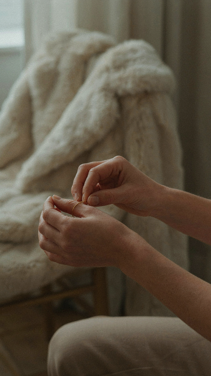 A woman puts on a delicate gold bracelet, with a faux fur coat nearby.