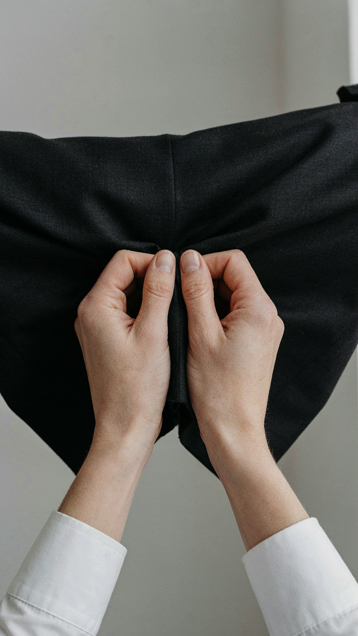Hands pinch black fabric, showing its elasticity and quick recovery.