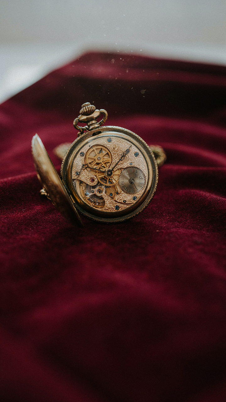 An antique pocket watch with exposed gears sits on a velvet cloth, showing timeless mechanics.